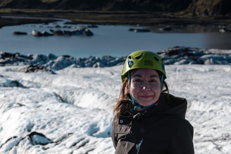 A woman with a green helmet smiles during her thrilling glacier hike