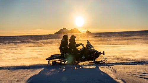 Snowmobilers racing across Langjökull glacier with mountain backdrop