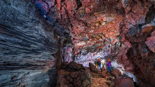 Explorers with headlamps walking through colorful lava tunnel