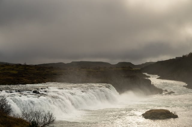 A man is fishing in front of a beautiful waterfall