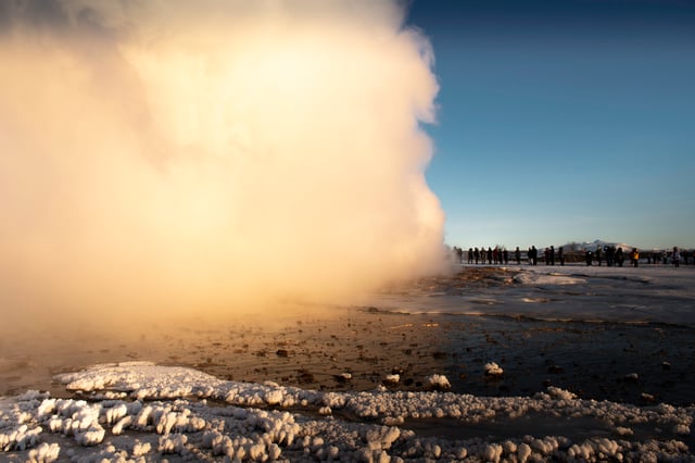 An icelandic geyser is blowing in front of a crowd on the golden circle