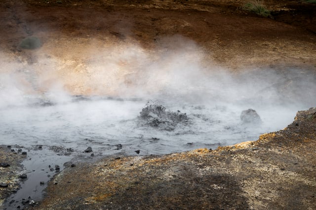 A nig puddle of mud, among sulfur colored rocks is boiling