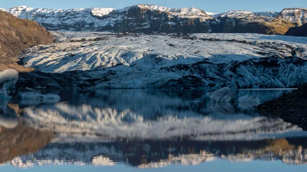 The mouth of the glacier Sólheimajökull is reflecting in the peaceful lake waters