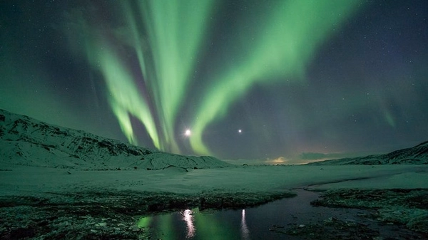 Dramatic Northern Lights reflection over Icelandic lake with mountain silhouettes