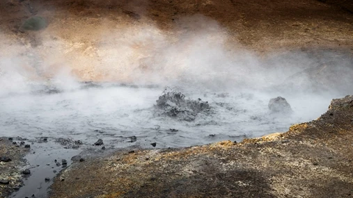 A nig puddle of mud, among sulfur colored rocks is boiling