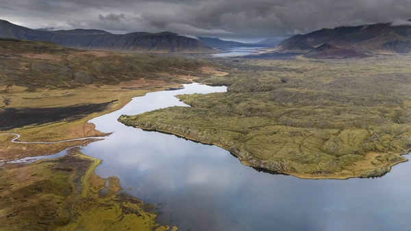 Lake bordering a beautiful red and green lava field in Berserkjahraun